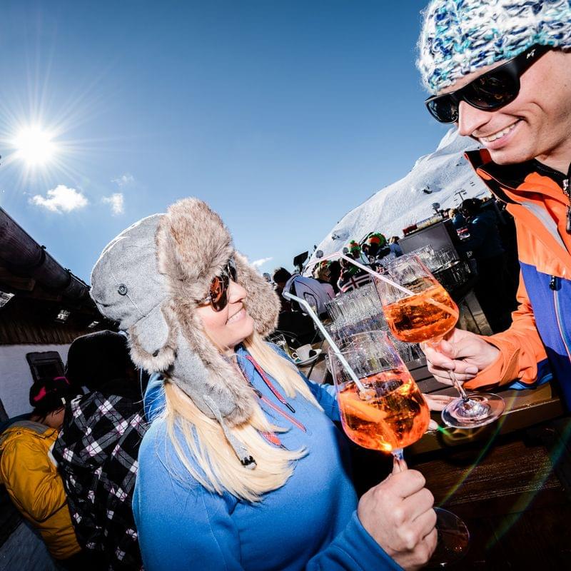 Paar trinkt Aperol Spritz bei Sonnenschein auf einer Skihütte in den Alpen